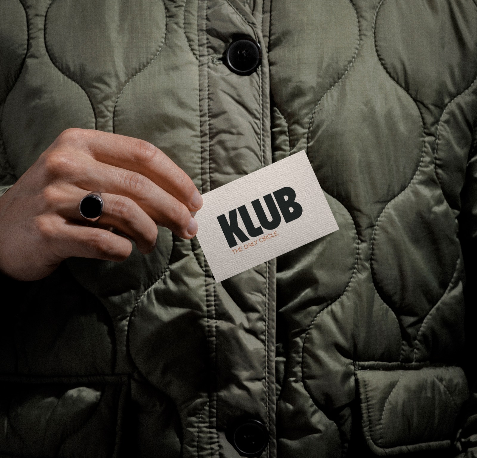 Carte de visite KLUB tenue devant une veste matelassée