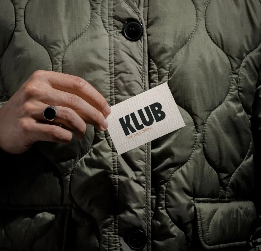 Carte de visite KLUB tenue devant une veste matelassée