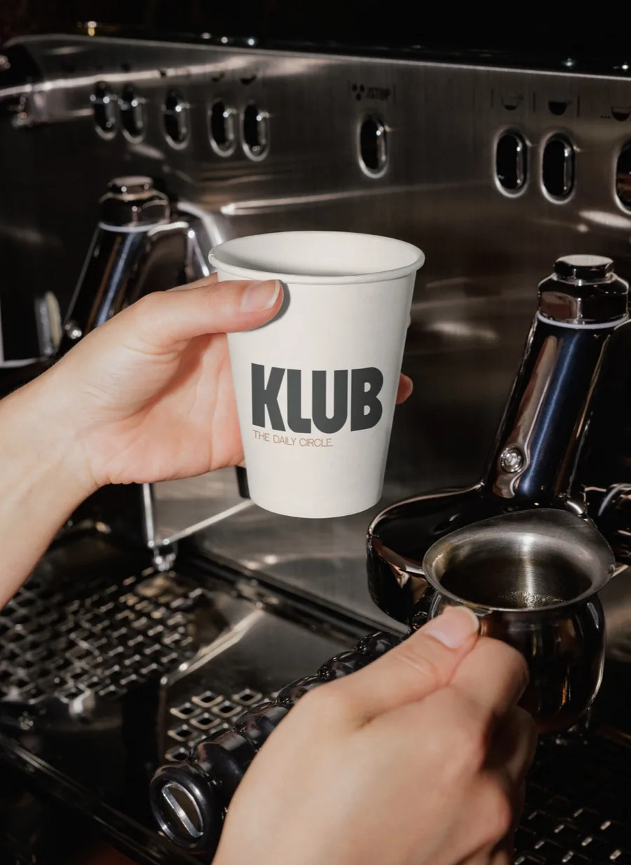 Gobelet KLUB tenu devant une machine à espresso