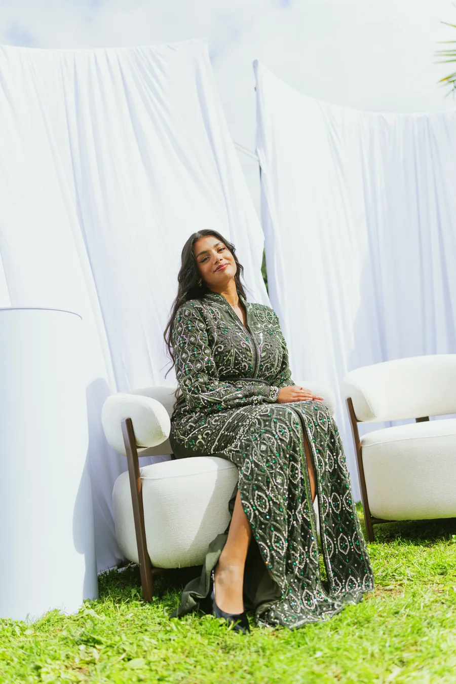 Portrait assis dans un fauteuil blanc, devant les tentures du décor