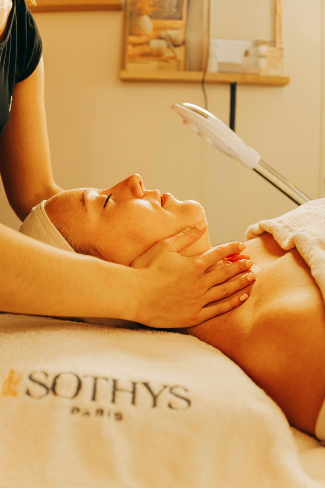 Soin du visage en institut, mains de l'esthéticienne sur les tempes, lumière chaude